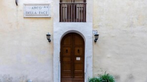 A building entrance with a double wooden door, a sign above reading "ARCO R.V. DELLA PACE", and a potted plant to the right. - Daplace - Emilia Apartment (Roma)