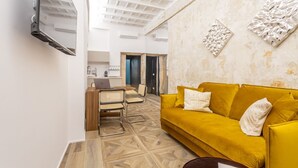 Een moderne woonkamer met een gele bank, een houten salontafel en een aan de muur bevestigde televisie.