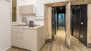 Een moderne keuken met een ingebouwde magnetron, een spoelbak en een koffiezetapparaat. Een gang leidt naar een slaapkamer met een gestreept dekbed.