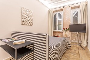 A modern room with a striped sofa, a small table with a book, a flat-screen TV, and a window with curtains. - Daplace - Elena Apartment (Roma)