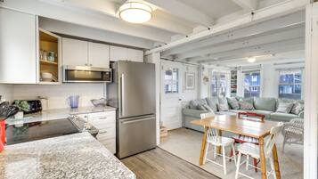 Una cocina moderna con gabinetes blancos, un refrigerador de acero inoxidable y un microondas. Hay una zona de comedor con una mesa de madera y sillas blancas.