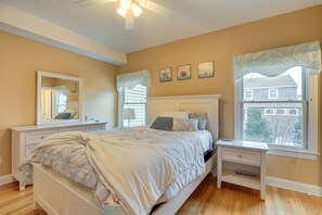 Un dormitorio con cama, mesitas de noche, cómoda, ventana con vistas y adornos en la pared.