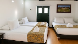 Ein Hotelzimmer mit drei Betten, jedes mit weißer Bettwäsche und einem gemusterten Überwurf. Eine grüne Tür und ein Gemälde sind an der Wand zu sehen.