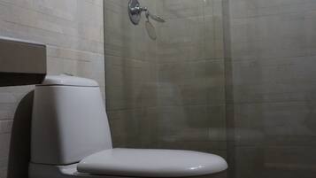Un baño con inodoro, cabina de ducha y una toalla en el suelo.