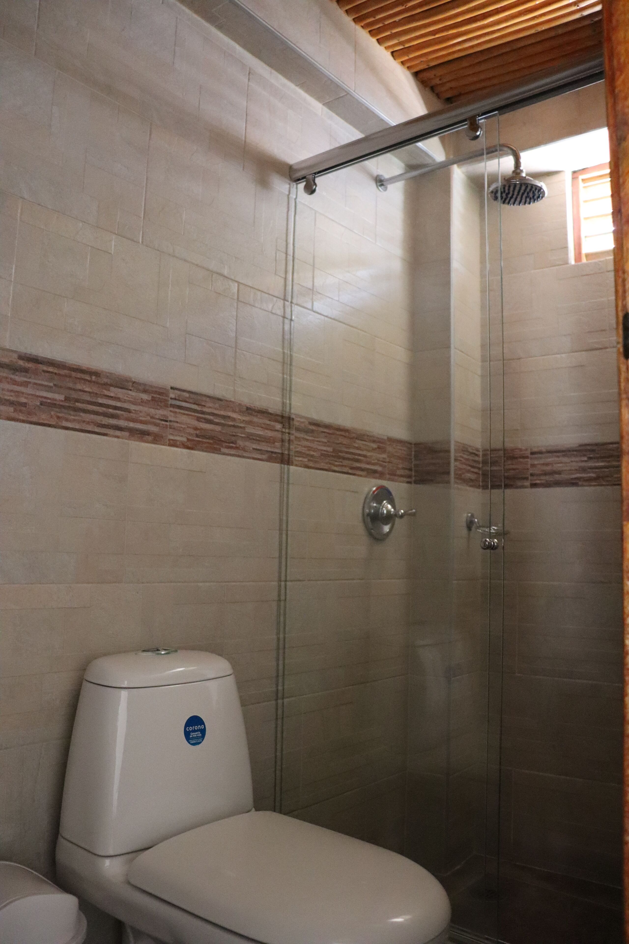 Un baño con inodoro, ducha con puerta de cristal y paredes de azulejos con un diseño de franja marrón.