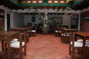 A restaurant with wooden tables and chairs, a tiled floor, and hanging plants.