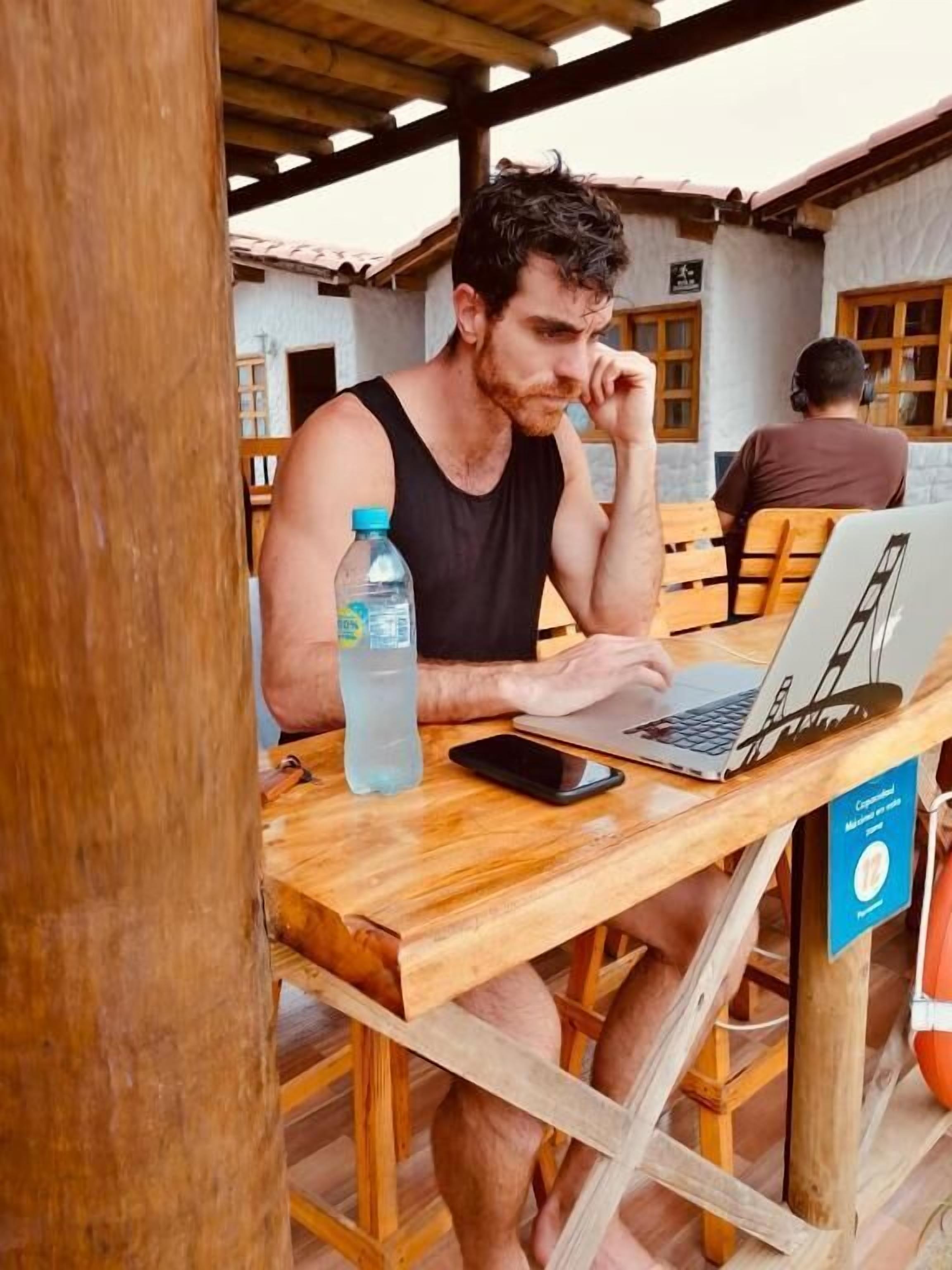 Iemand zit aan een houten tafel met een laptop, een smartphone, een waterfles en een bord dat 12% korting aangeeft.