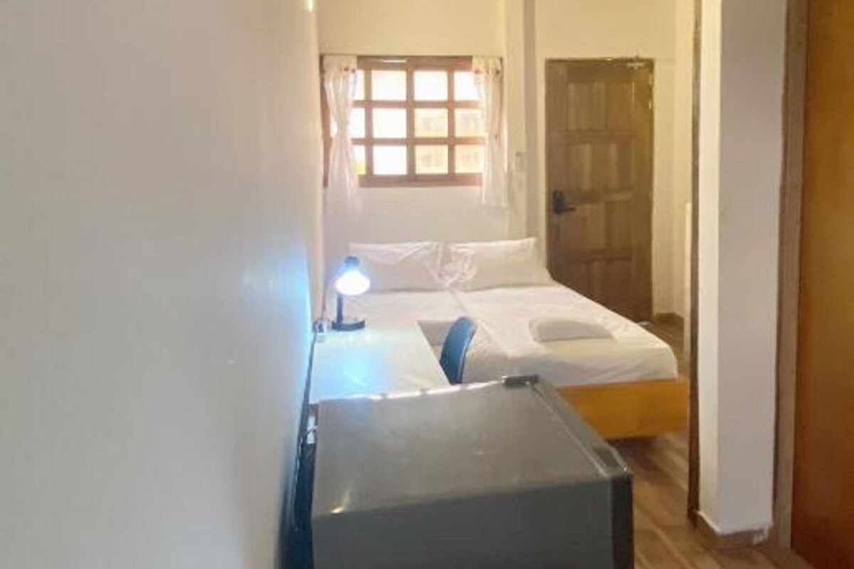 A bedroom with a bed, a bedside table, a lamp, and a wooden floor.