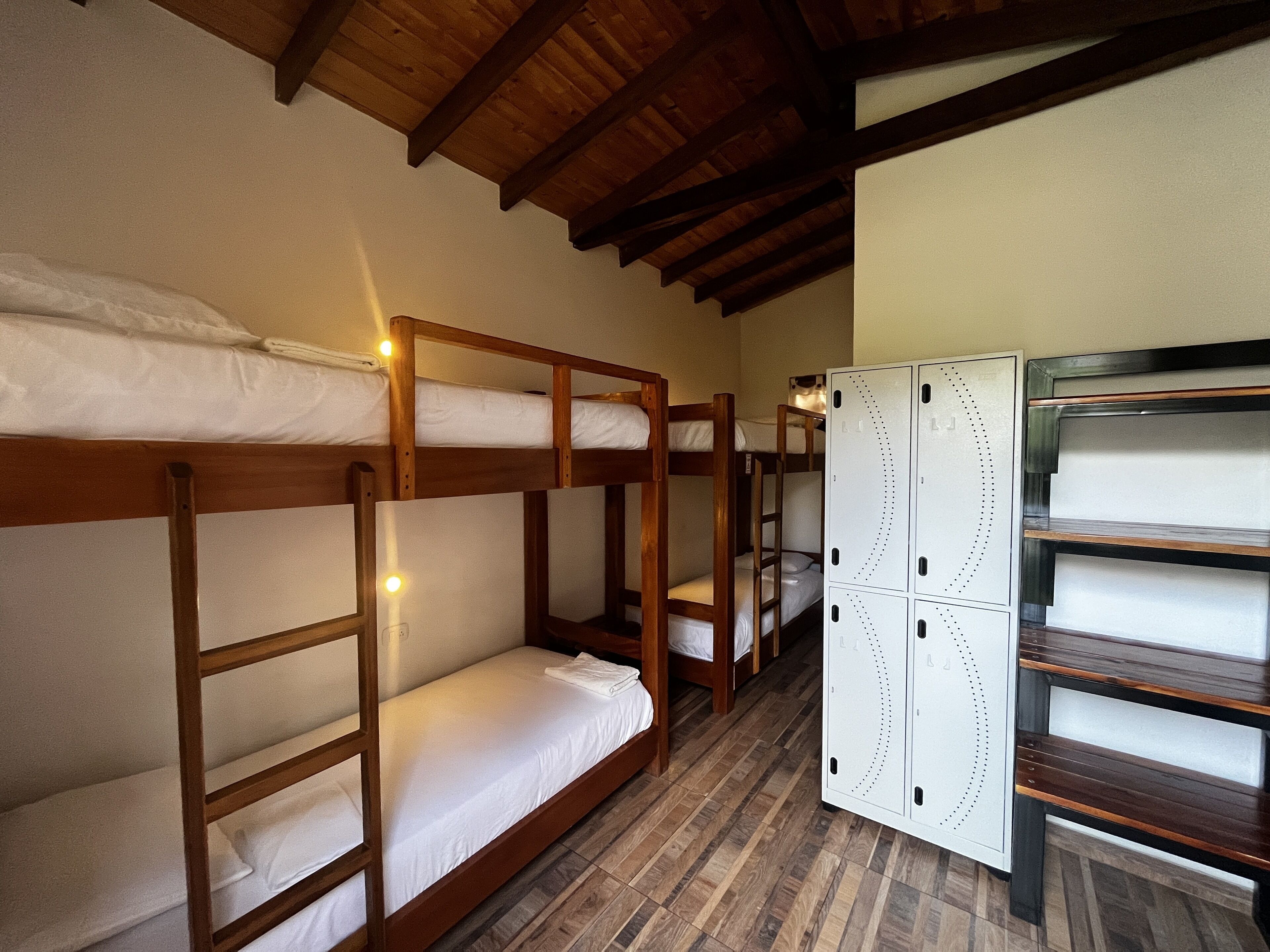 Bunk beds with wooden frames and white bedding, a white wardrobe with dotted patterns, and a wooden ceiling.