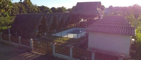 A traditional thatched-roof building with a swimming pool and a fenced area.