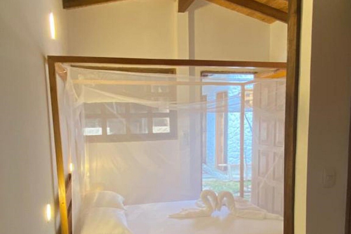 Una cama con dosel, suelo de madera y ventana con vistas al verdor.