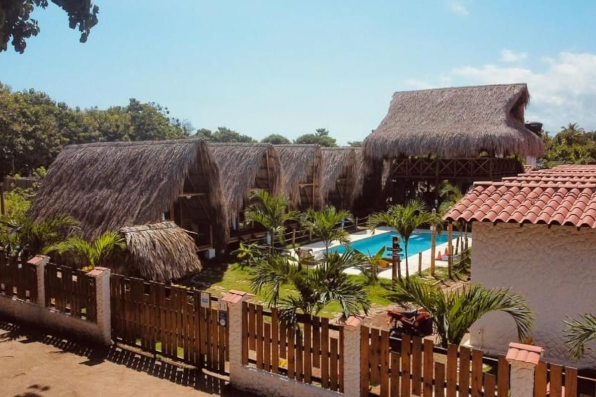 A resort with thatched-roof buildings, a swimming pool, and palm trees.