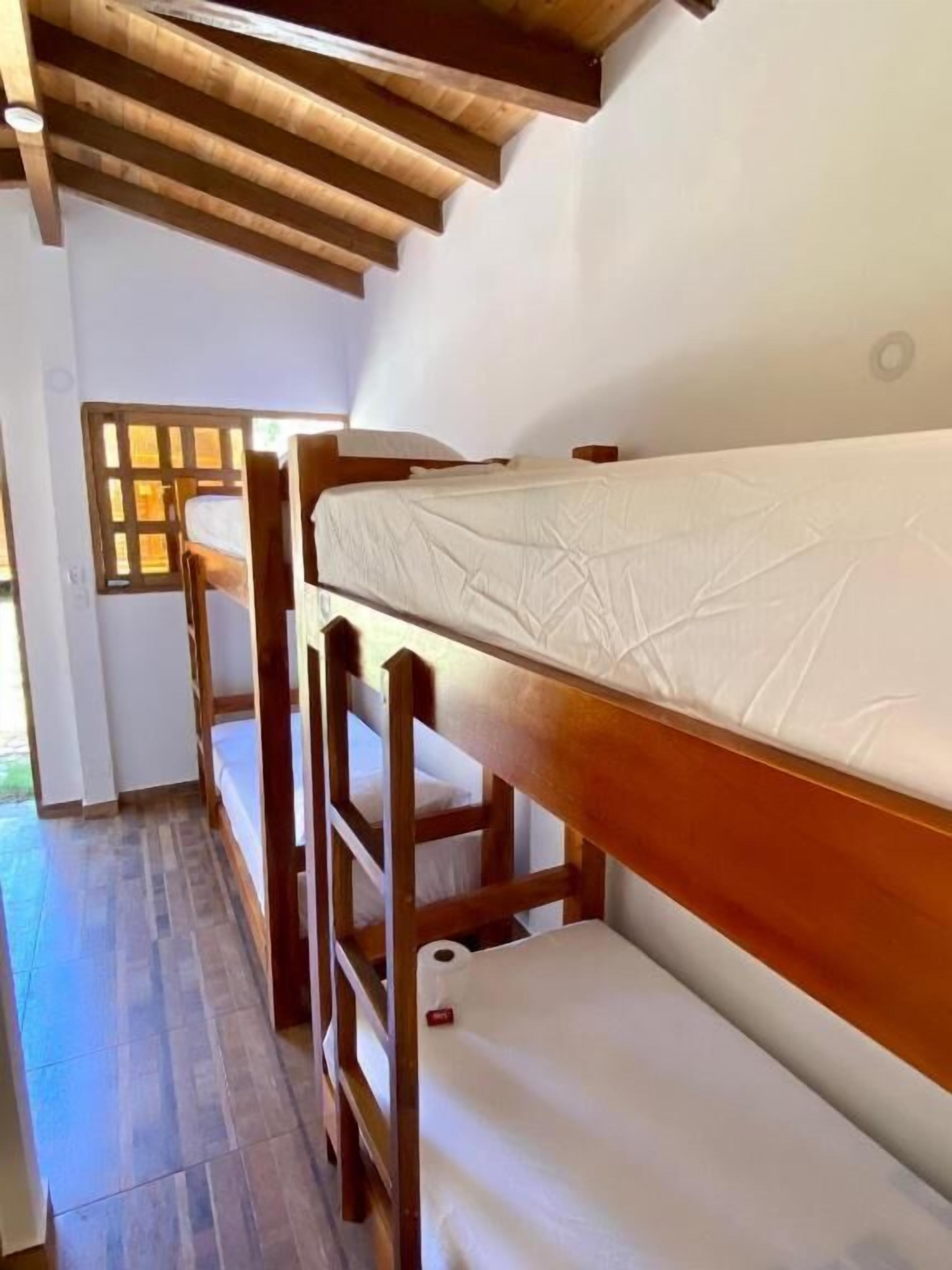 Une rangée de lits superposés en bois, avec des matelas blancs, un plancher en bois et un plafond en bois.