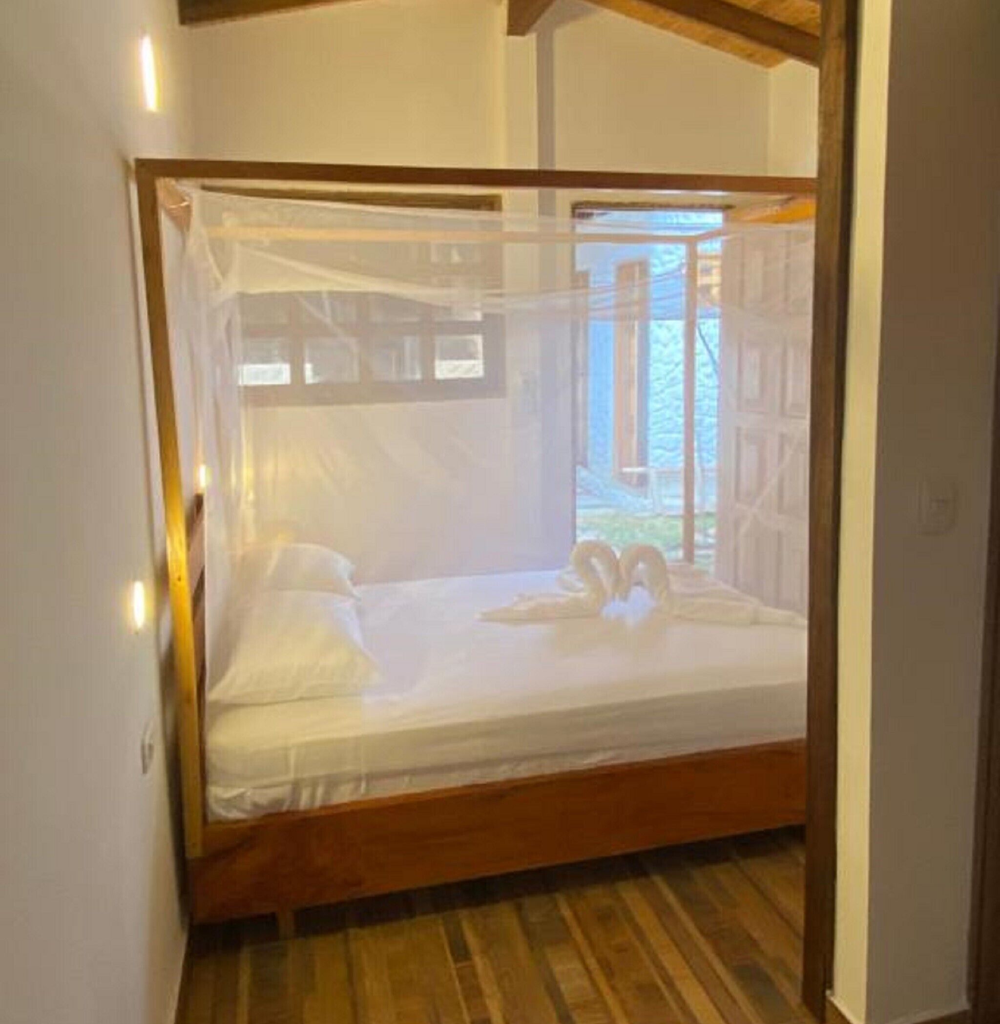 Un letto a baldacchino, pavimento in legno e una finestra vista su vegetazione.