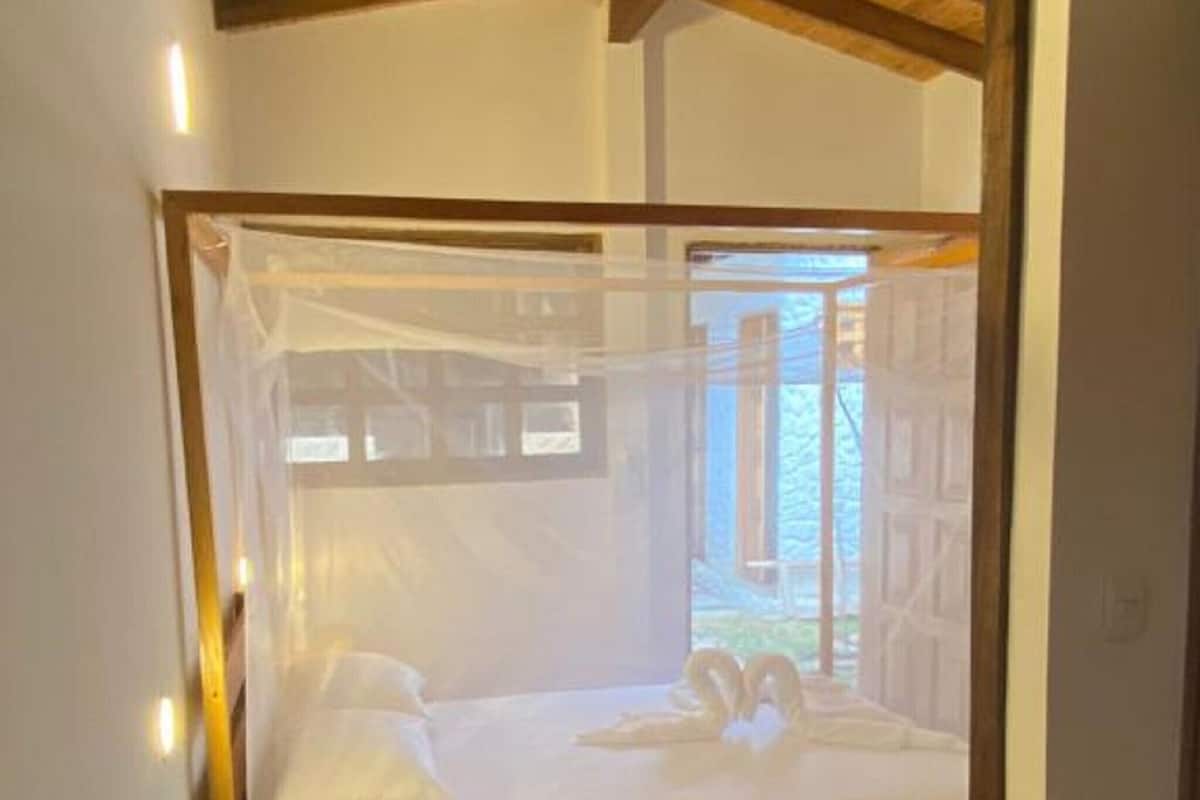 Ein Bett mit Baldachin, Holzboden und ein Fenster mit Blick auf Grünflächen.