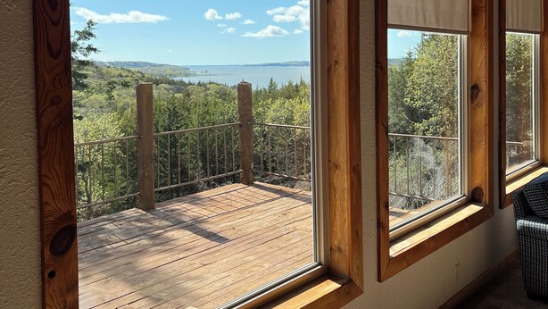 Huone, jossa on suuret ikkunat, joista avautuu näkymä puukannelle ja järvelle.