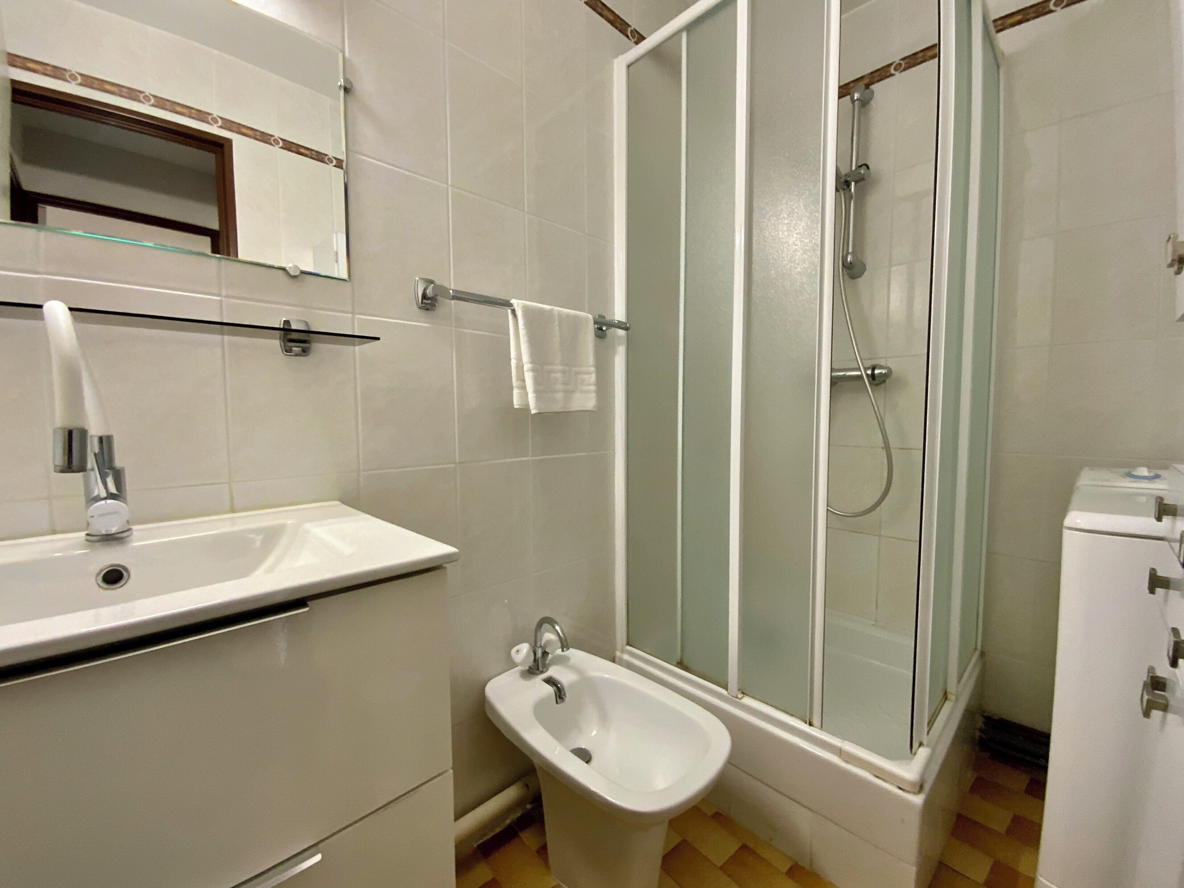 Un baño con lavamanos, bidé y ducha con mampara de vidrio.
