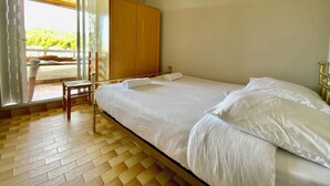 Un dormitorio con cama, un armario de madera, una silla y vistas al exterior a través de un ventanal.