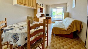 Una habitación con una cama, una mesa con un periódico, armarios de madera y un televisor.