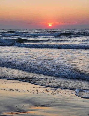 Un coucher de soleil sur l’océan, avec des vagues qui se rapprochent du rivage.