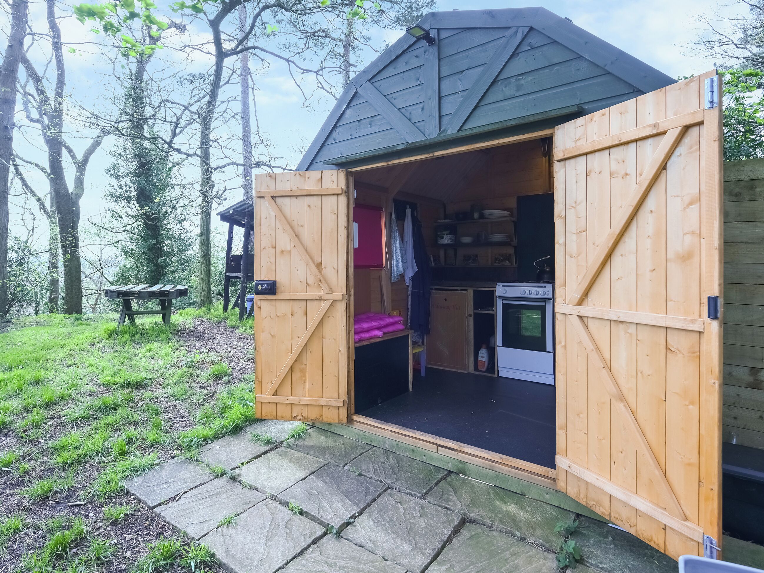 A wooden structure with a kitchen area, including a stove and cabinets, and a bench outside.