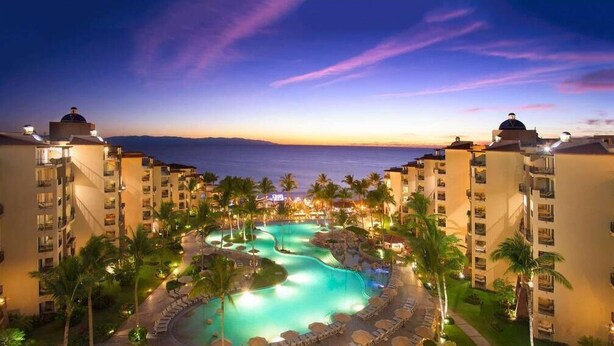 A resort with a swimming pool surrounded by palm trees and beachfront views.