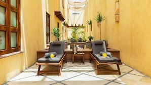 A narrow hallway with two lounge chairs and a small table, surrounded by yellow walls and a tiled floor.