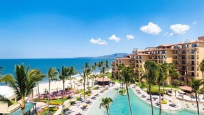 A resort with a pool, palm trees, and a view of the ocean.