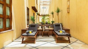 A narrow hallway with two lounge chairs and a small table, surrounded by yellow walls and a tiled floor.