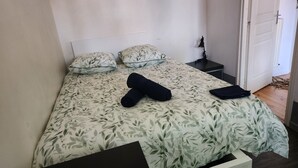 Een bed met een bloemenbedekking, twee kussens, een opgerolde handdoek en een klein nachtkastje met een lamp.