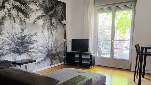 Een moderne woonkamer met een bank, een televisie op een dressoir en een groot raam met uitzicht op de omgeving.
