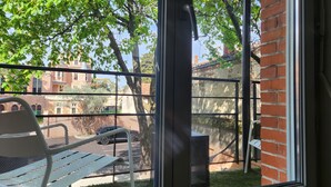 Een balkon met een metalen stoel en tafel, met uitzicht op een bakstenen gebouw en bomen.