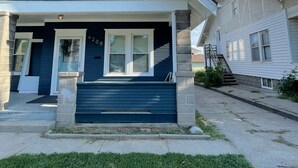Een tweelaags huis met een donkerblauwe gevel, witte sierlijsten en een veranda met een stenen zuil.