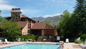 Ein Poolbereich mit einem Steinhaus, Sitzgelegenheiten im Freien und Bergen im Hintergrund.