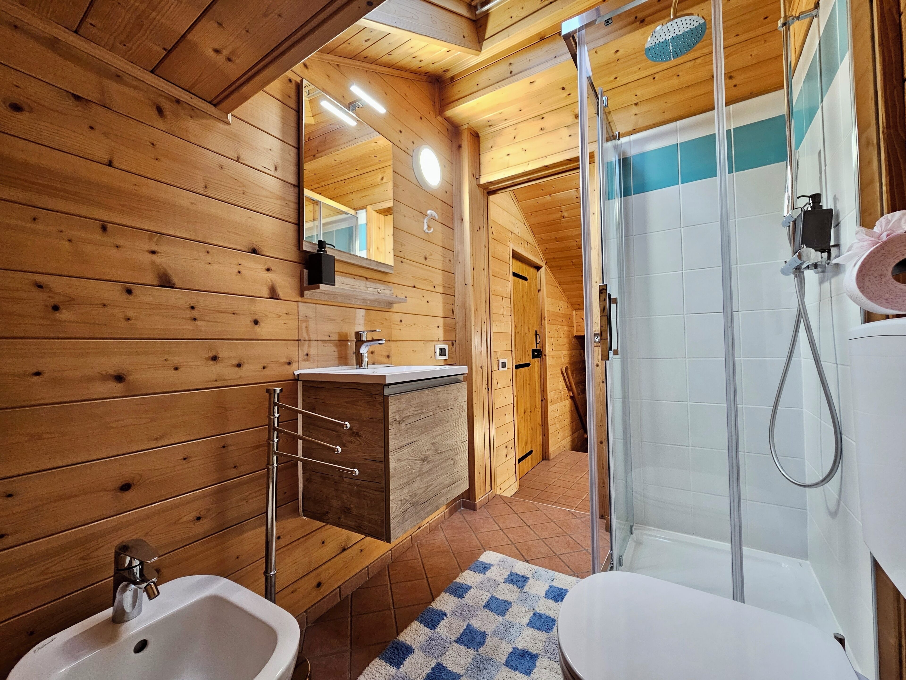 Arredamento in legno con bagno dotato di lavabo, specchio e doccia.