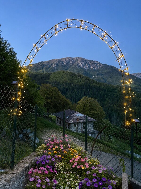 Paisaje montañoso con una casa y un arco decorativo con luces.