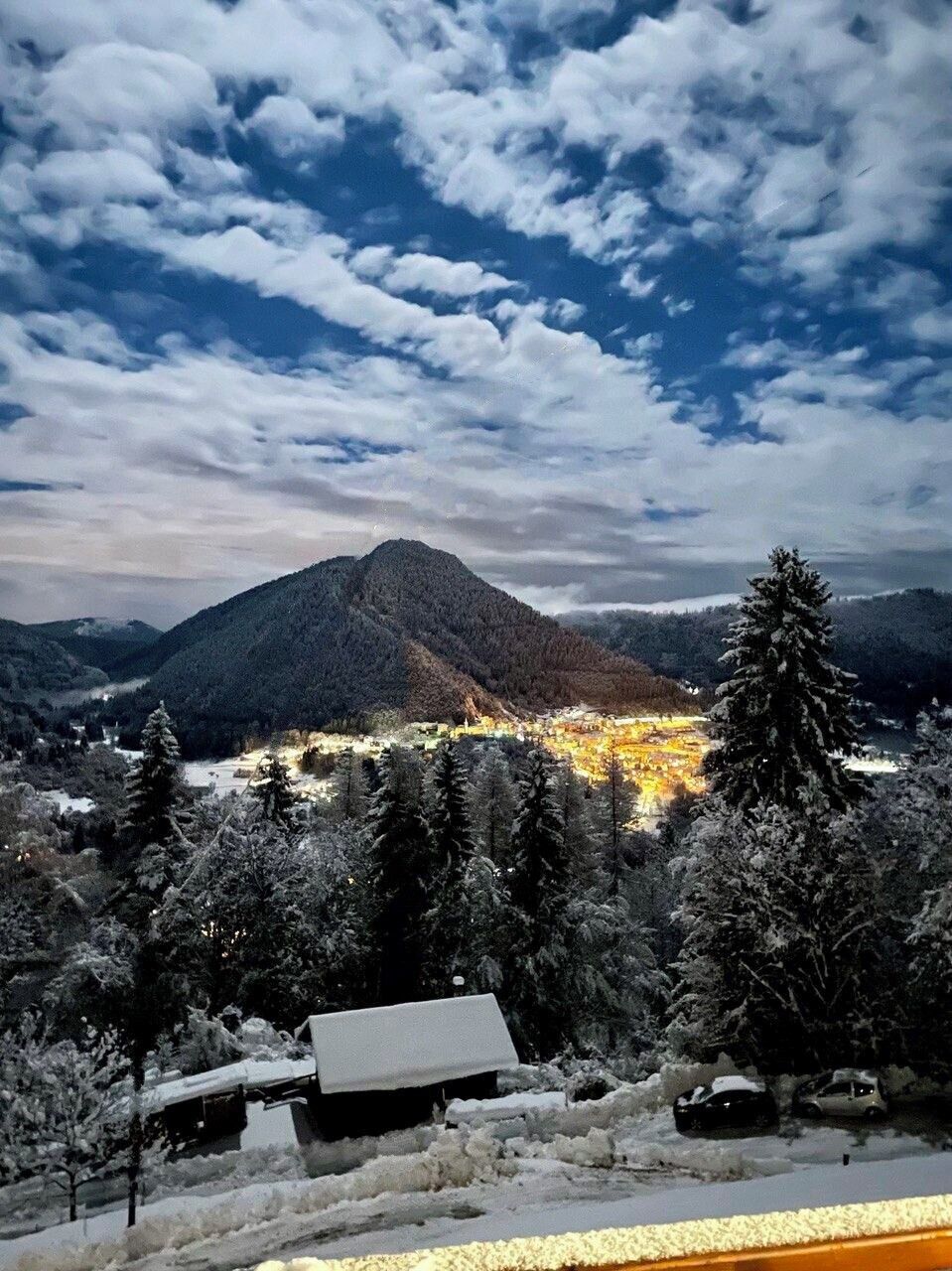 Paesaggio montuoso con una città nella valle, alberi coperti di neve e cielo sereno.