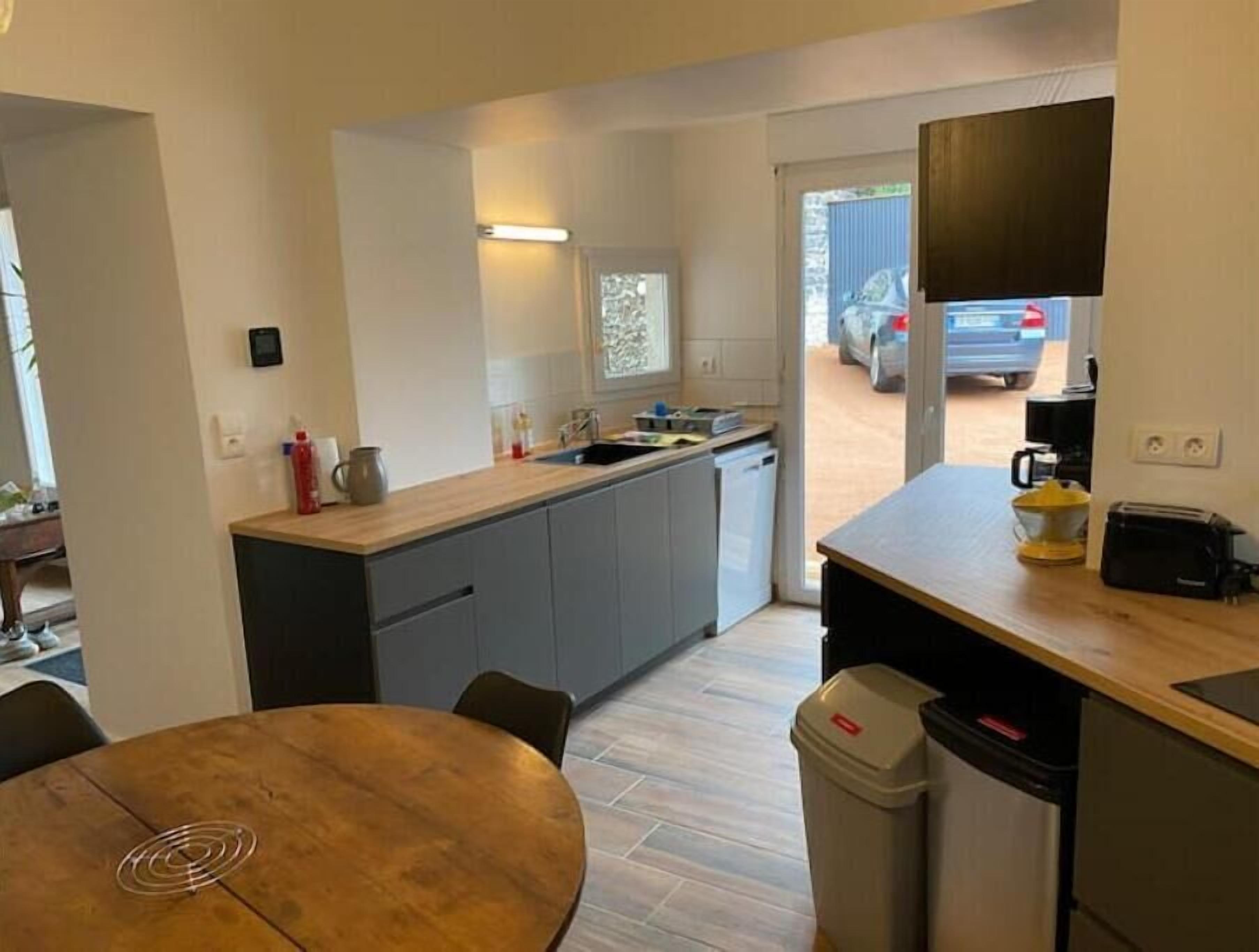 Cocina compacta con armarios grises, encimera de madera, un lavamanos y una zona de comedor con una mesa redonda.
