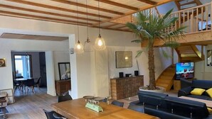 Uma sala de estar ampla com uma mesa de jantar de madeira, cadeiras pretas, um sofá preto e uma grande planta em vaso.
