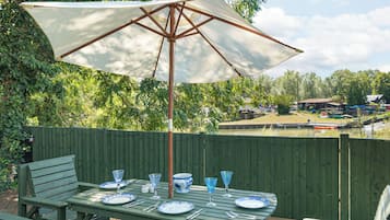Un espace extérieur aménagé pour les repas, avec une table dressée pour quatre personnes, un grand parasol et une vue sur les bateaux et la verdure en arrière-plan.