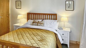 Un lit bien fait, recouvert d’une courtepointe matelassée, deux lampes de chevet, une tête de lit en bois, une table de chevet blanche et des tableaux encadrés accrochés au mur.