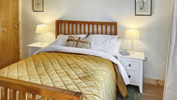 Un lit bien fait, recouvert d’une courtepointe matelassée, deux lampes de chevet, une tête de lit en bois, une table de chevet blanche et des tableaux encadrés accrochés au mur.