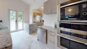 A modern kitchen with a dishwasher, double oven, and a marble countertop.