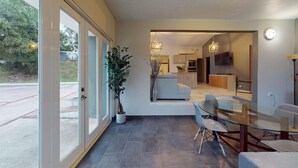 A modern interior with a glass dining table, chairs, a sofa, and a potted plant.