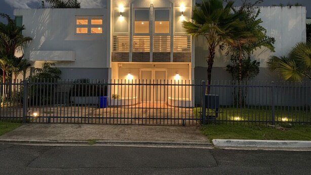 A modern building with a gated entrance, multiple windows, and a well-lit facade. - Hidden Paradise w/ Pool (Guaynabo)