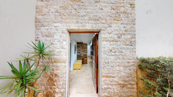 A stone-walled corridor with a wooden door, potted plants, and a bench. - Unique and Luxurious 5 Bedroom Mansion (Río)