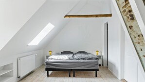 Quarto com teto inclinado, uma cama, um radiador e um claraboia.