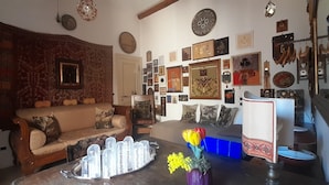 Un salon chaleureux avec un canapé, une table basse agrémentée d’objets décoratifs et un mur orné de divers tableaux et horloges encadrés.