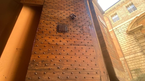 Une porte en bois ornée de clous métalliques et munie d’un petit loquet métallique.