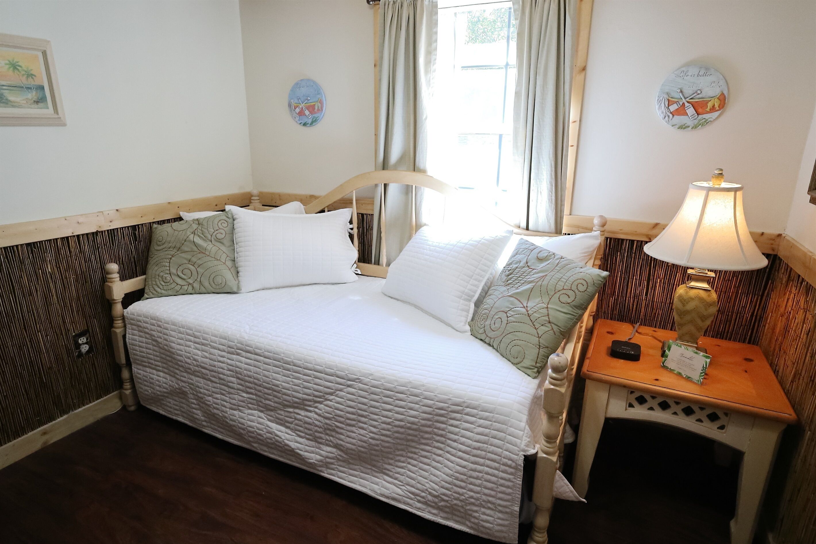 Een bed met een witte quilt, een houten hoofdbord en een nachtkastje met een lamp en een klein decoratief item.